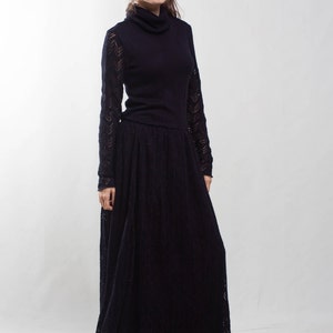 K&ouml;nnte beinhalten: Eine Frau tr&auml;gt ein schwarzes, lang&auml;rmeliges Kleid mit hohem Kragen und einem Spitzenmuster. Das Kleid hat einen flie&szlig;enden Rock und sie tr&auml;gt schwarze Abs&auml;tze.
