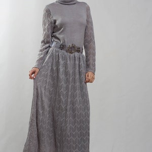 May include: A gray knitted dress with a long skirt and a decorative belt. The dress has a turtleneck and a chevron pattern.