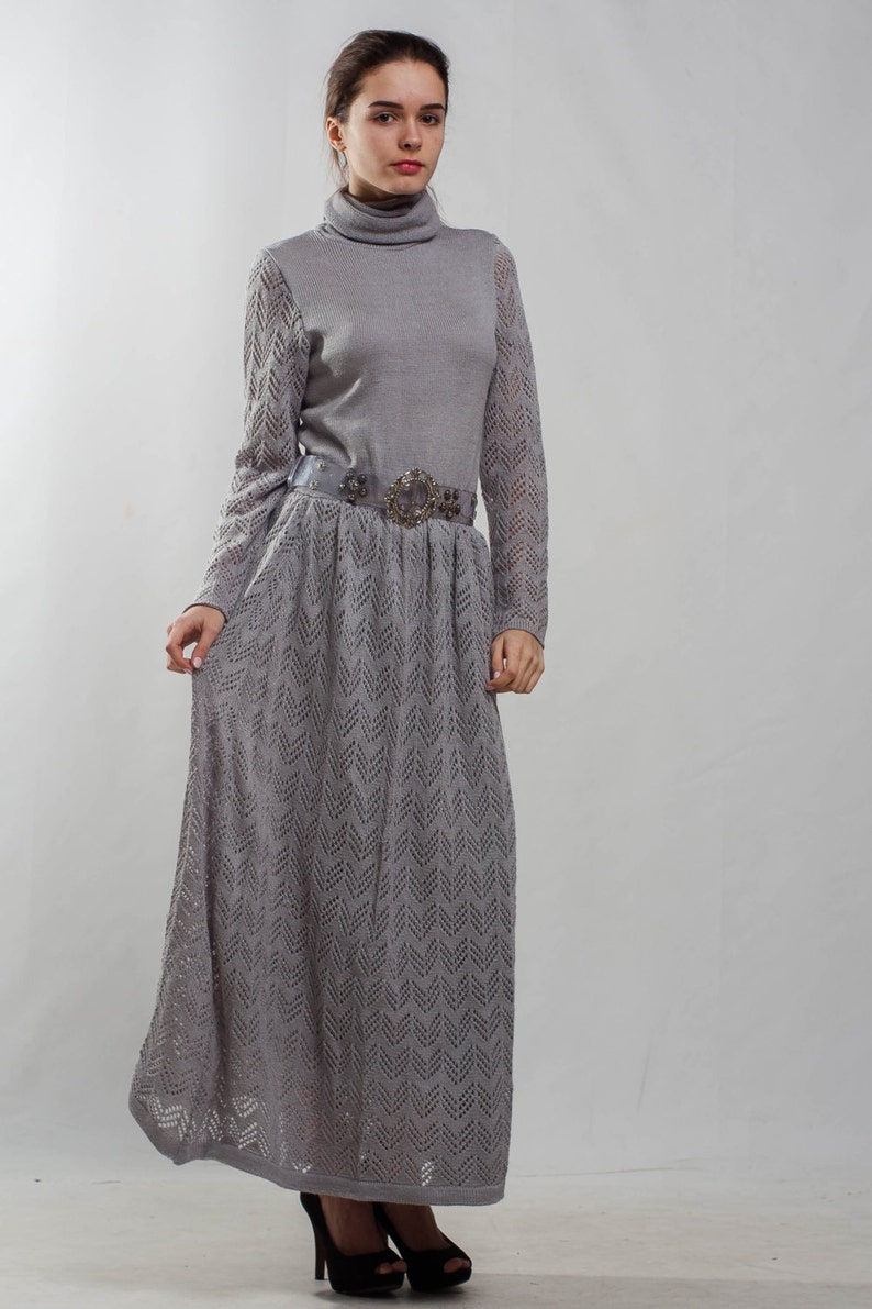 May include: A gray knitted dress with a long skirt and a decorative belt. The dress has a turtleneck and a chevron pattern.