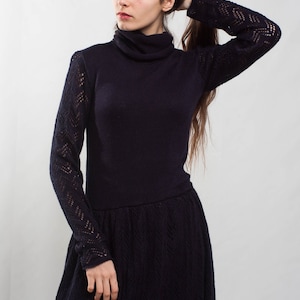 K&ouml;nnte beinhalten: Eine Frau tr&auml;gt ein langes, dunkelblaues Strickkleid mit Rollkragen und einem Spitzenmuster an den &Auml;rmeln.