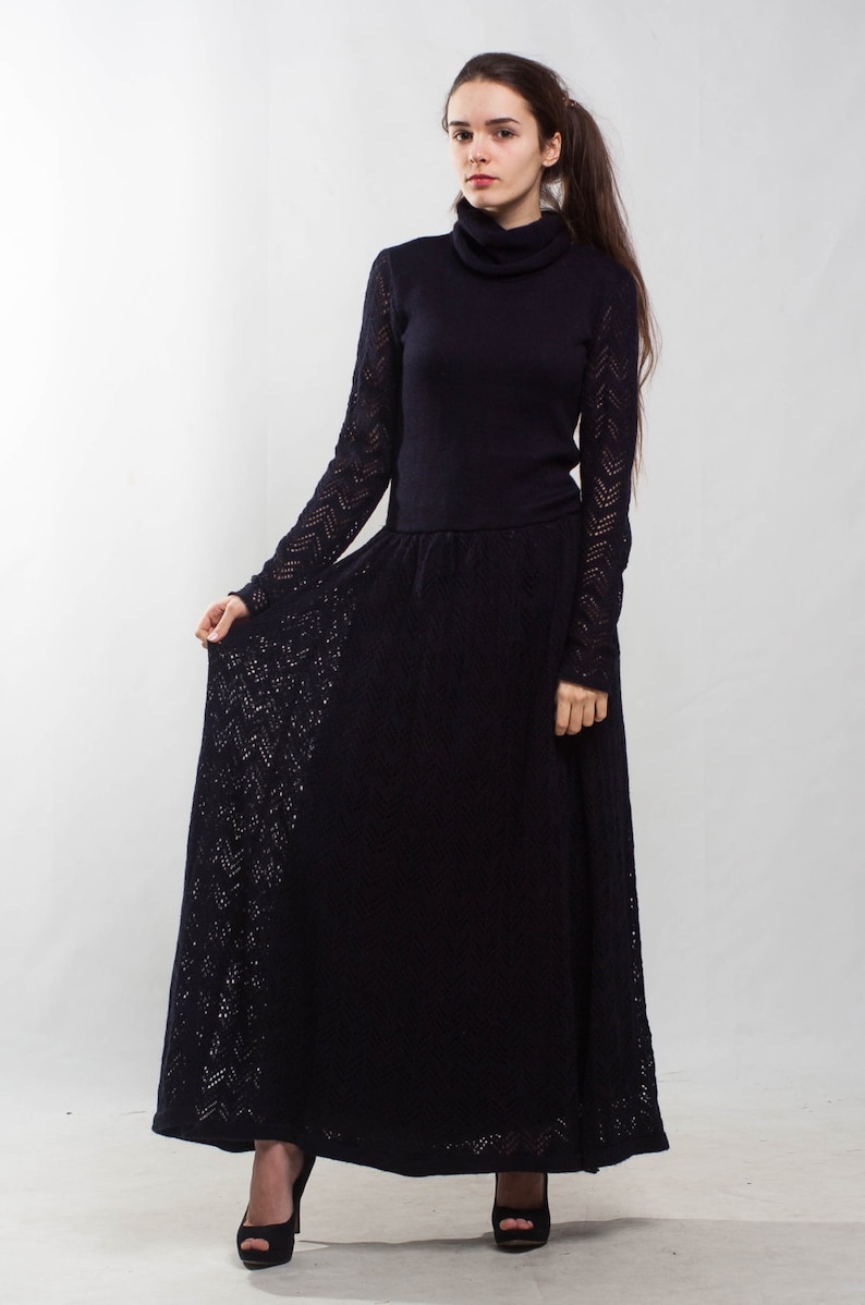 K&ouml;nnte beinhalten: Ein langes schwarzes Strickkleid mit Rollkragen und einem spitzem Muster. Das Kleid ist am Oberk&ouml;rper figurbetont und geht in einen weiten Rock &uuml;ber.