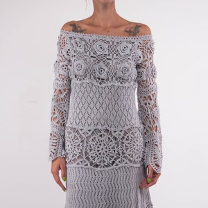 May include: A gray crochet maxi dress with a delicate floral pattern. The dress has a loose fit and long sleeves.