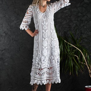May include: A white crochet dress with a long, flowing skirt and a delicate floral pattern. The dress has a V-neckline and three-quarter sleeves.