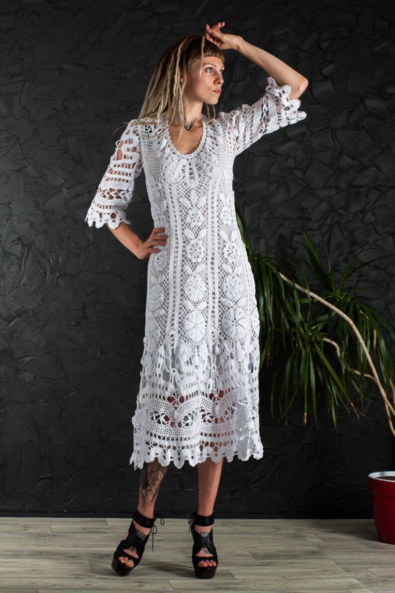 May include: A white crochet dress with a long, flowing skirt and a delicate floral pattern. The dress has a V-neckline and three-quarter sleeves.