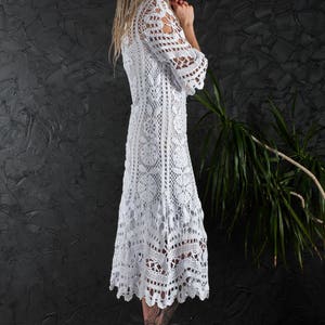 May include: A white crochet dress with a long, flowing skirt and a fitted bodice. The dress is made with a delicate lace pattern and has a scalloped hemline.