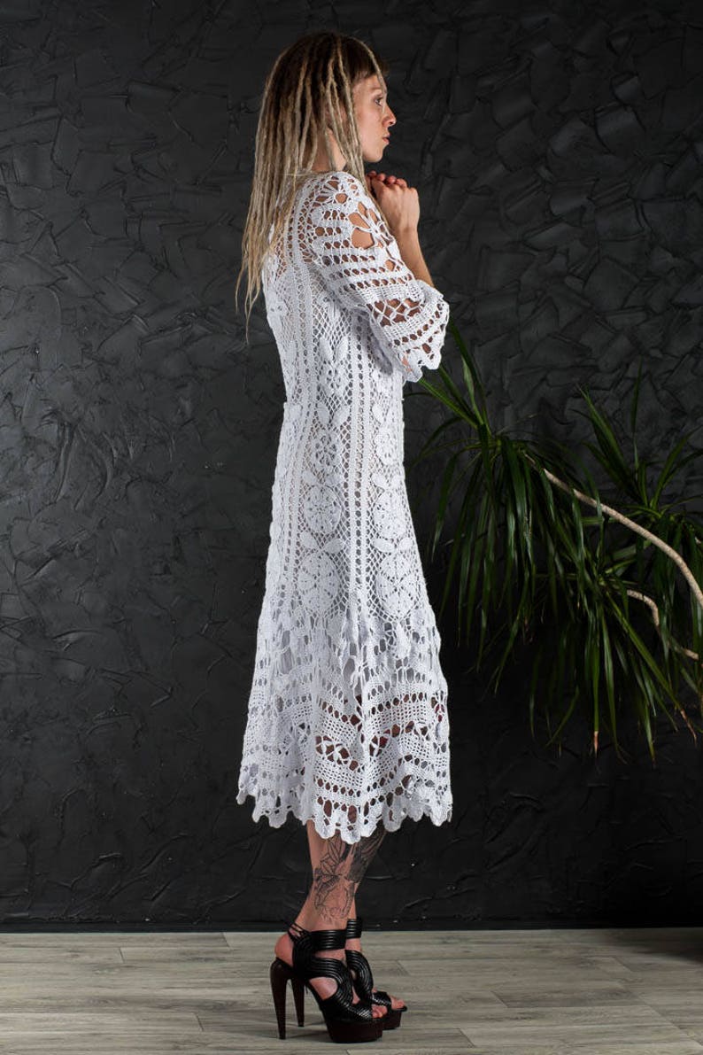May include: A white crochet dress with a long, flowing skirt and a fitted bodice. The dress is made with a delicate lace pattern and has a scalloped hemline.
