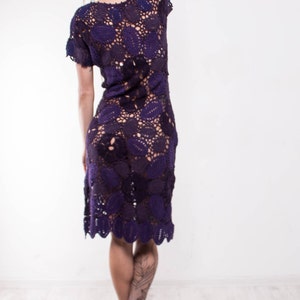 May include: A woman wearing a purple crochet dress with a floral pattern. She has blonde dreadlocks and is wearing black high heels.