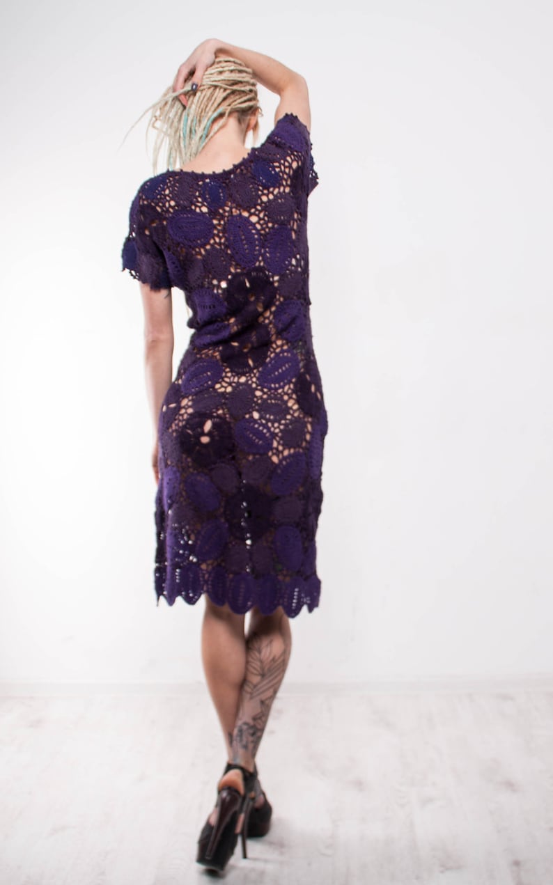 May include: A woman wearing a purple crochet dress with a floral pattern. She has blonde dreadlocks and is wearing black high heels.