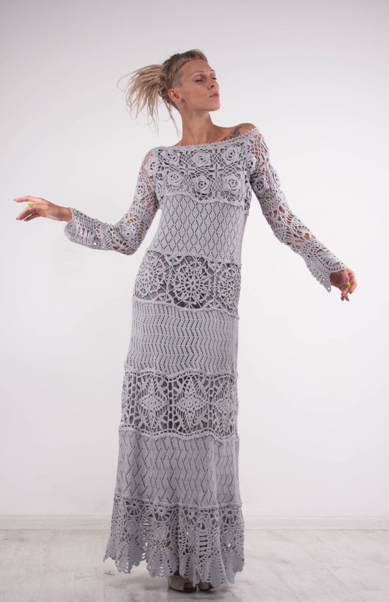 May include: A long, gray crochet dress with a loose fit and a flowing skirt. The dress features a variety of crochet patterns, including flowers, diamonds, and circles.