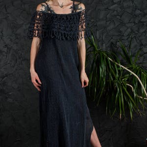 May include: A long, black crochet dress with a lace overlay and a side slit. The dress is worn by a person with tattoos and is styled with black high heels.