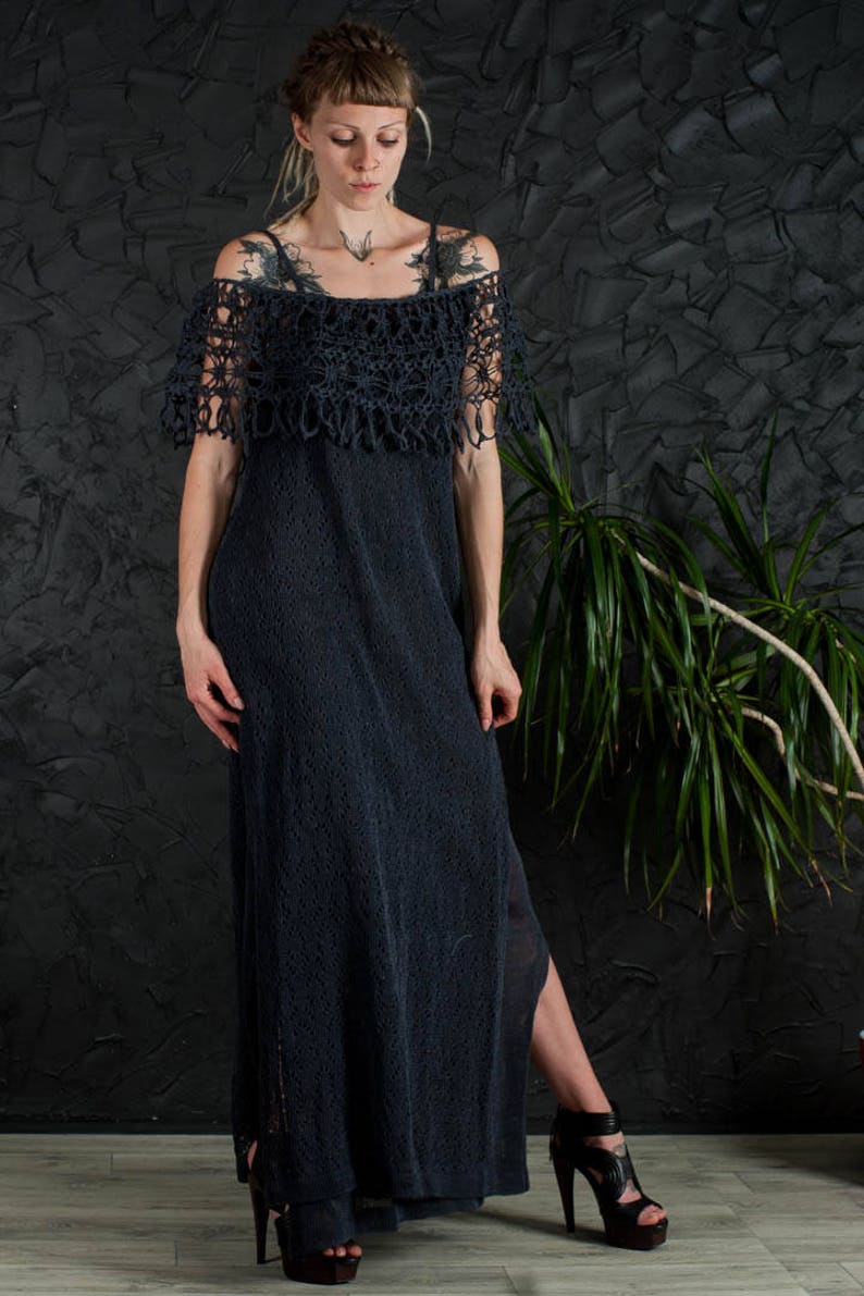 May include: A long, black crochet dress with a lace overlay and a side slit. The dress is worn by a person with tattoos and is styled with black high heels.