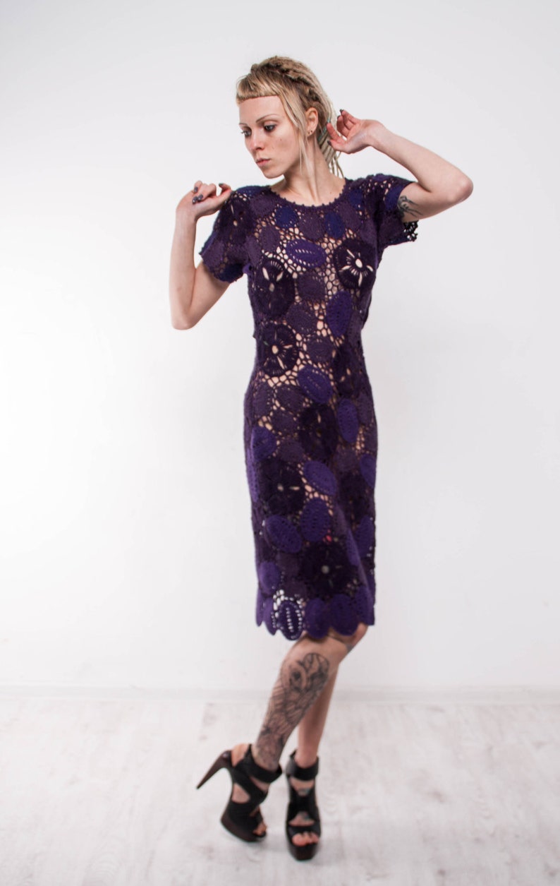 May include: A woman wearing a purple crochet dress with a floral pattern. She is wearing black high heels and has a tattoo on her leg.