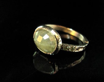 May include: A gold ring with a large, oval-shaped green gemstone set in a bezel setting. The band is textured and has smaller green gemstones set into it.