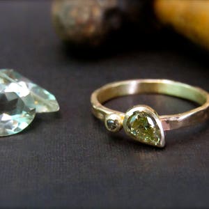 May include: A gold ring featuring a pear-shaped green gemstone and a smaller round black gemstone. The ring is displayed against a black backdrop.