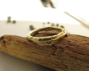 May include: A simple gold band ring with a textured finish. The ring is sitting on a piece of driftwood.