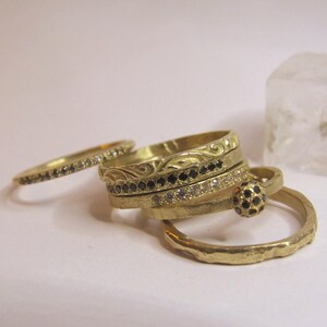 May include: A selection of gold rings with different designs. Some rings are adorned with black and white gemstones, while others have textured or engraved surfaces. A clear, cube-shaped object is in the background.