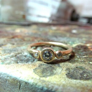 May include: A gold ring with three round diamonds set in a textured band.