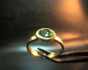 May include: A gold ring with a green gemstone set in a bezel setting.