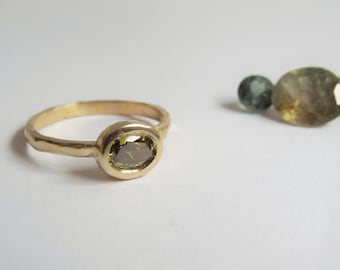May include: A gold ring with a textured band and a bezel setting featuring a green gemstone.