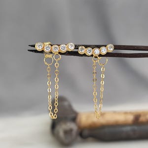 May include: A pair of gold earrings with a row of small clear stones and a dangling chain.
