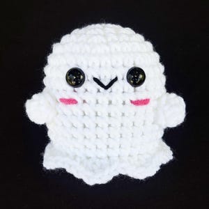 May include: White crocheted ghost plush toy with black eyes and pink cheeks. The ghost has a small, stitched-on mouth.