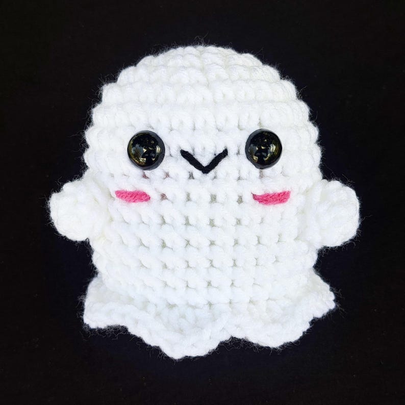 May include: White crocheted ghost plush toy with black eyes and pink cheeks. The ghost has a small, stitched-on mouth.