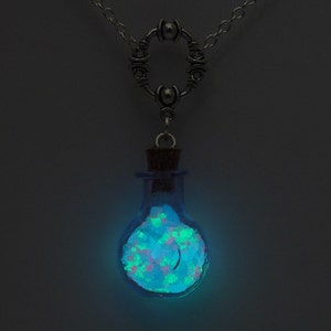 May include: A silver chain necklace with a round pendant featuring a small glass bottle filled with glowing green and pink glitter.