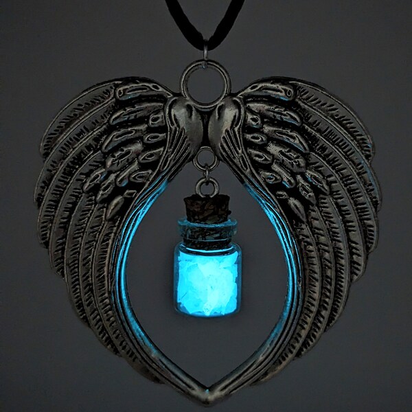 May include: A silver pendant necklace with a heart-shaped frame featuring two angel wings. A small glass vial filled with glowing blue crystals hangs from the center of the heart.