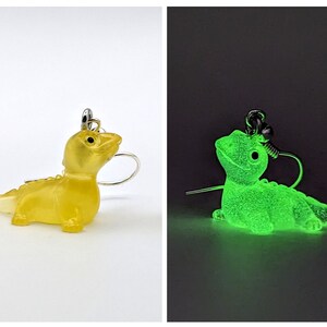May include: A pair of earrings featuring a yellow lizard-like creature with a silver hook. The earrings glow green in the dark.