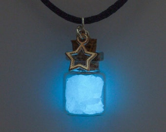 May include: A blue glow-in-the-dark powder inside a small glass bottle with a cork stopper and a silver star charm. The bottle is hanging from a black cord.