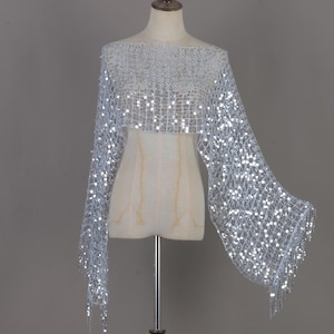 May include: A silver sequinned bolero shrug featuring an open-knit mesh construction with wide, flared sleeves. The garment is adorned with numerous reflective circular sequins throughout the fabric, creating a shimmering effect across the entire piece.