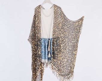 May include: A gold sequined sheer cover-up with fringe detailing. The cover-up is hanging on a white hanger against a white background.