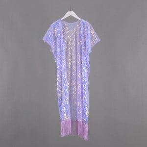 May include: A long, light purple sequined cardigan with a fringe hem. The cardigan has short sleeves and is hanging on a white hanger.