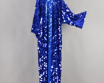 May include: A long, open-front robe with a vibrant blue sequin design. The robe features wide sleeves and a floor-length cut, hanging from a white hanger against a neutral background. The sequins create a shimmering effect, perfect for special occasions.