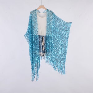 Puede incluir: Una estola azul claro con lentejuelas y detalles de flecos. La estola está hecha de una tela transparente y tiene un corte holgado y fluido.