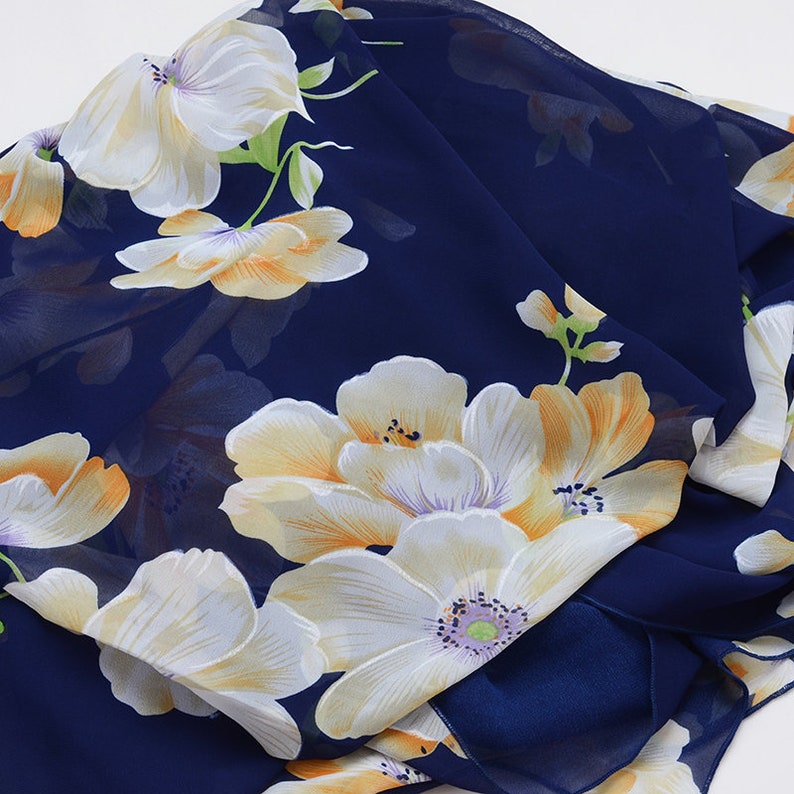May include: A navy blue chiffon scarf with a floral print featuring white and yellow flowers.