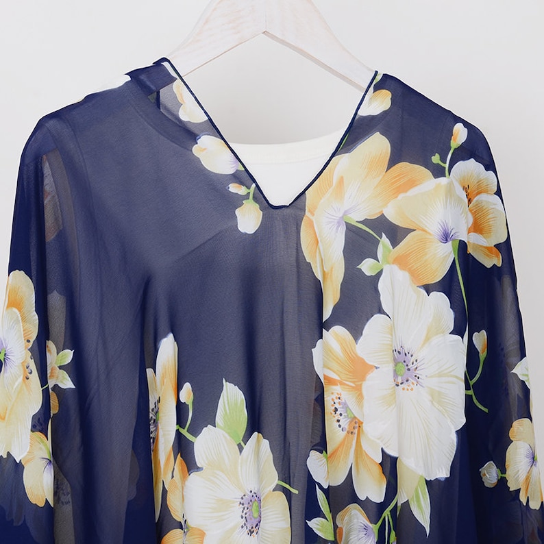 May include: A navy blue sheer top with a floral print featuring yellow and white flowers. The top has a V-neck and a relaxed fit.