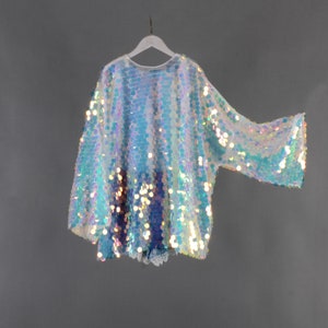 May include: A white iridescent sequin top with long sleeves. The top has a loose fit and a round neckline.