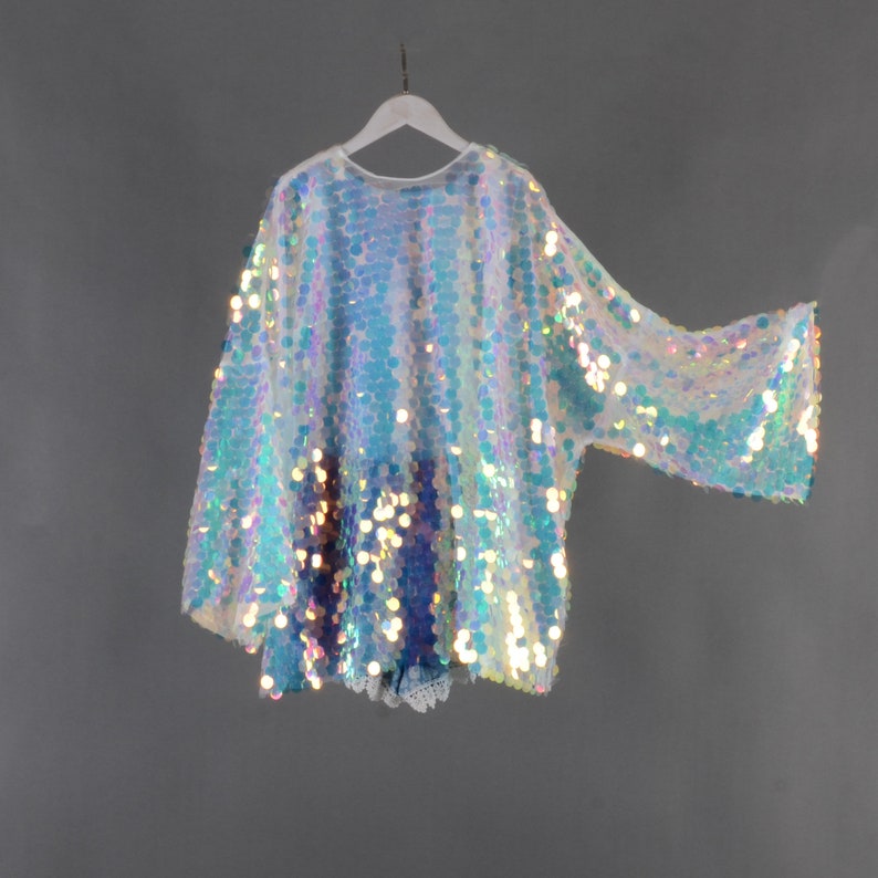 May include: A white iridescent sequin top with long sleeves. The top has a loose fit and a round neckline.
