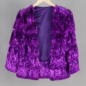 May include: A purple metallic fringe jacket with a layered design. The jacket is open in the front and has a silky lining.