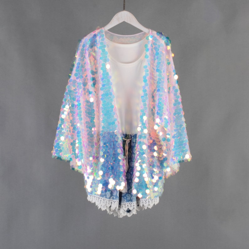 Op de afbeelding: Een regenboogkleurig sequined vest met een losse pasvorm en 3/4 mouwen. Het vest is gemaakt van een transparante stof en heeft een lichtroze en blauwe kleurstelling.