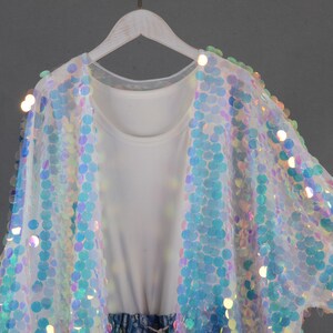 May include: A white sheer cardigan with iridescent sequins in a circular pattern. The cardigan has a relaxed fit and is perfect for layering.