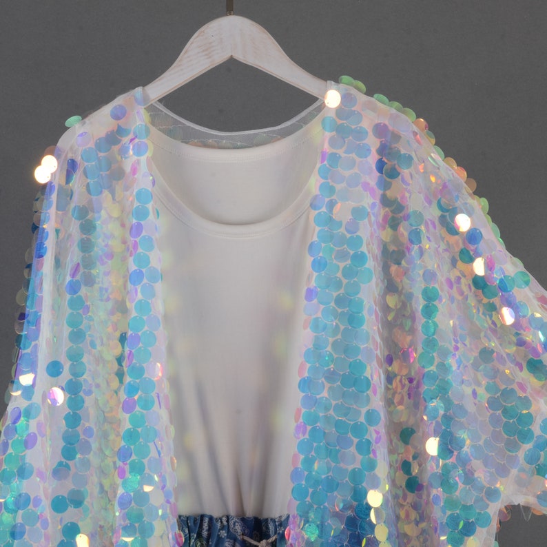 May include: A white sheer cardigan with iridescent sequins in a circular pattern. The cardigan has a relaxed fit and is perfect for layering.