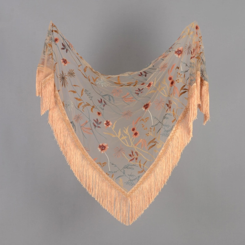 May include: A sheer, triangular scarf with embroidered floral patterns in shades of red, orange, and yellow. The scarf has a peach-colored fringe trim along the edges. The scarf is a delicate accessory.