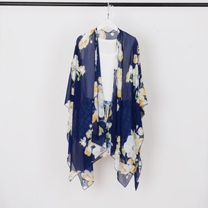 May include: A navy blue floral chiffon kimono with yellow and white flowers. The kimono is hanging on a white hanger against a white background.
