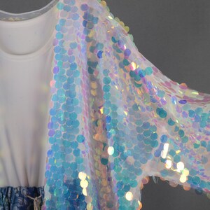 May include: A sheer iridescent white cardigan with sequins. The sequins are round and have a rainbow effect.