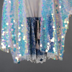 May include: A white iridescent sequined jacket with a blue and white patterned skirt underneath. The skirt has a white lace trim.