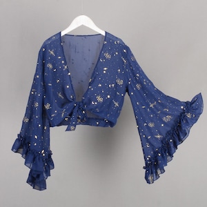 Op de afbeelding: Een marineblauw crop top met lange mouwen en een strik aan de voorkant. De top is bedekt met een gouden sterren- en halvemaanpatroon.