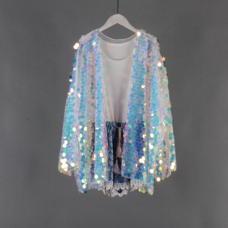 May include: A sheer iridescent sequined cardigan with long sleeves. The cardigan is white with blue and iridescent sequins.