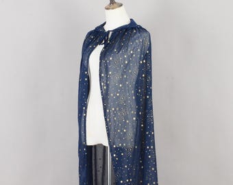 May include: A floor-length navy blue sheer cape featuring a pattern of metallic gold stars of varying sizes. The garment has a hood and a tie closure at the neck, draped over a white mannequin torso to display the translucent fabric.